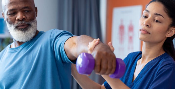 Diverse female physiotherapist helping senior male patient exercise with dumbbell, copy space. Hospital, medical and healthcare services.