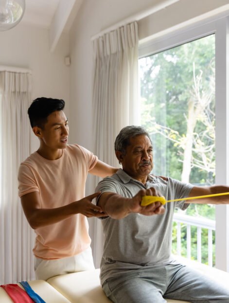 Happy diverse male physiotherapist advising and senior male patient using exercise band. Physiotherapy, healthcare, wellbeing, and senior lifestyle, unaltered.